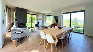 Een moderne woonkamer met een eethoek, grote ramen en een open haard.