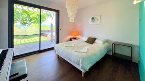 Een slaapkamer met een bed, een piano, een kroonluchter, een lamp en uitzicht op groen.