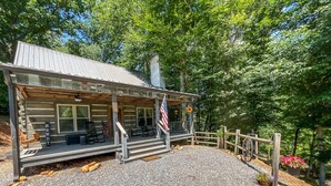 Une cabane rustique avec une véranda, un drapeau américain et une clôture en bois.
