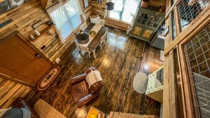 L’intérieur d’une cabane est doté d’un plancher en bois, d’un coin repas avec une table et des chaises, d’un canapé en cuir, d’une petite armoire et d’une fenêtre avec des rideaux.