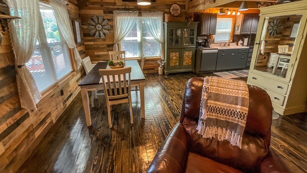 L’intérieur d’un chalet rustique comprend un coin repas, un canapé en cuir, une cuisine et une grande fenêtre agrémentée de rideaux.