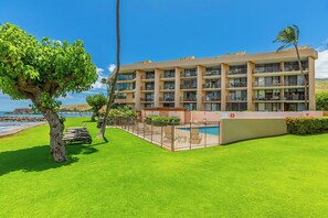 A multi-story hotel with a pool, surrounded by well-maintained grass and palm trees.