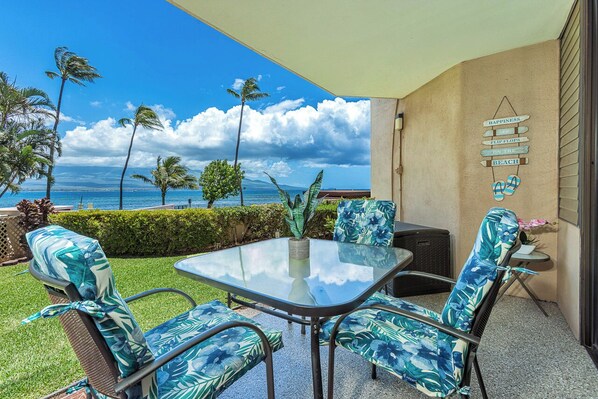 A patio with a glass table and chairs, a view of the ocean, and a sign on the wall.