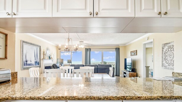 A modern kitchen with granite countertops, white cabinetry, and a dining area with a gray sofa and white chairs.
