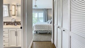 Un dormitorio con cama, mesita de noche, espejo y ventana con cortinas.