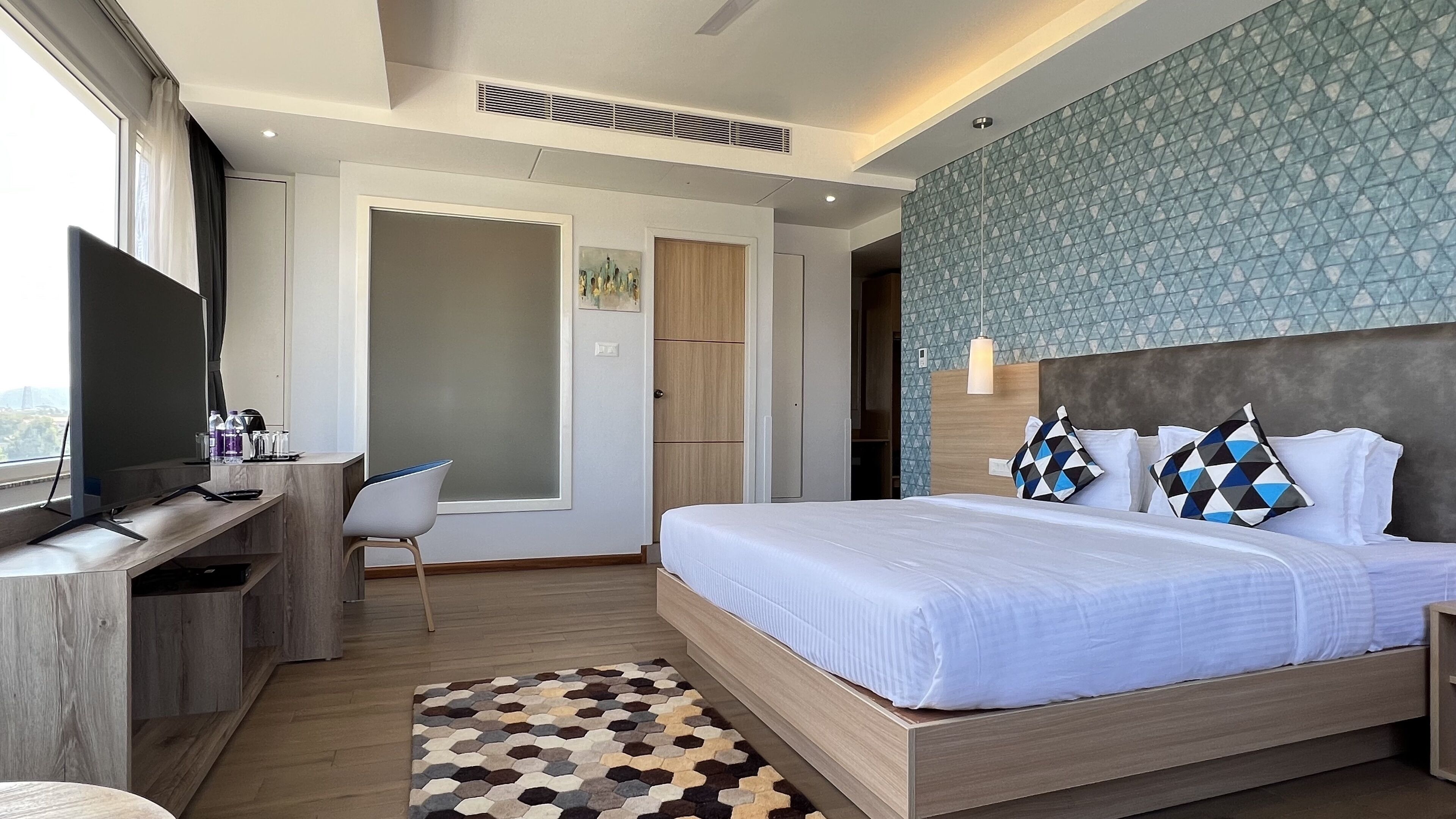 Habitación de hotel moderna con una cama grande, un escritorio con televisor y vista a la ciudad.