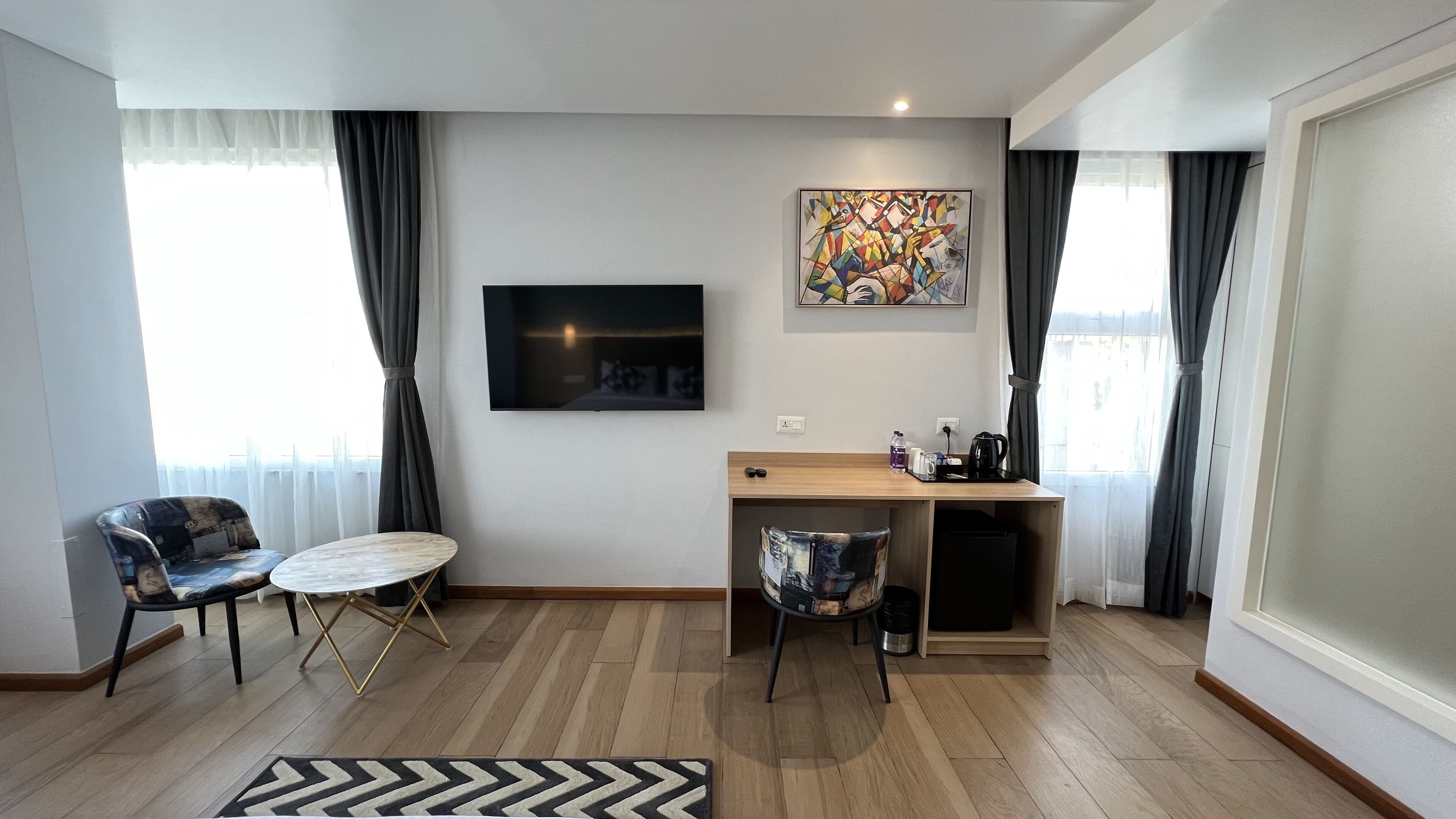Ein modernes Wohnzimmer mit Fernseher, einem Gemälde, einem Schreibtisch mit Stuhl und einer Kaffeemaschine.