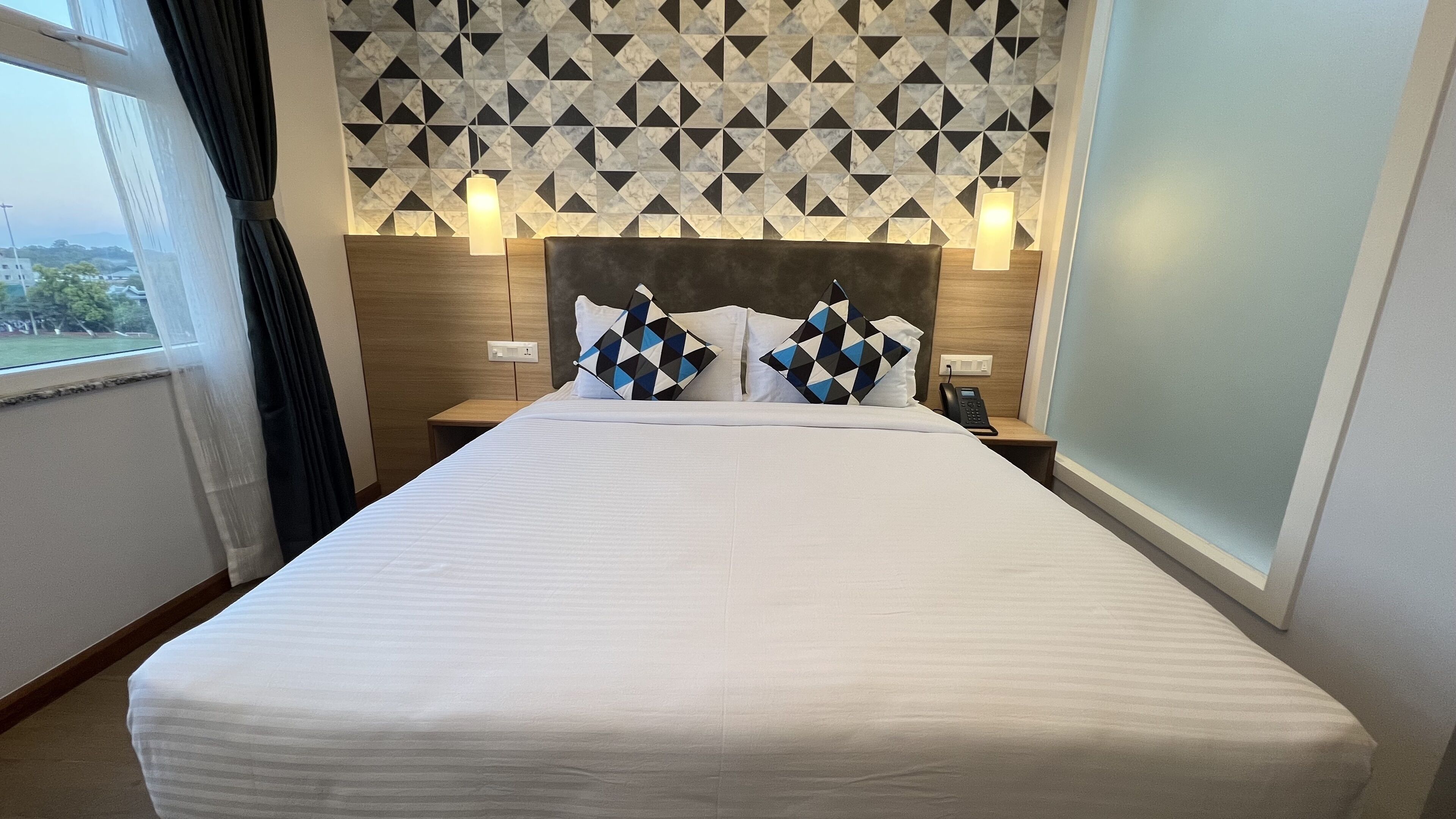 Une chambre d’hôtel avec un lit, deux tables de chevet, un téléphone et une vue sur l’extérieur.