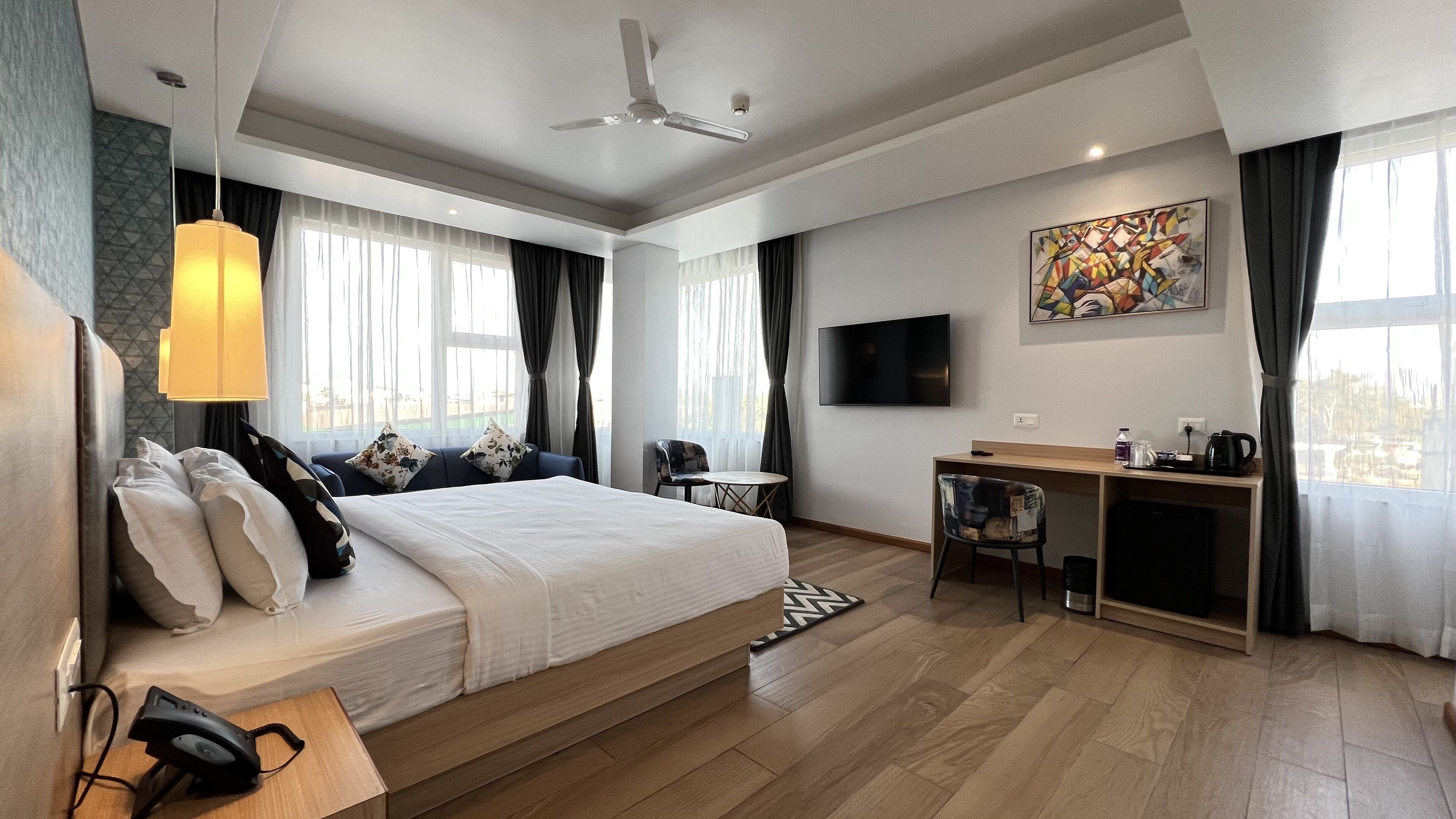 Una habitación de hotel moderna con una cama grande, un escritorio, una silla, un televisor y un cuadro en la pared.