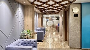 A modern lobby with a marble floor, grey upholstered seating, wooden ceiling beams, and a central air conditioning unit. - Aurora Boutique Hotel (Imphal)