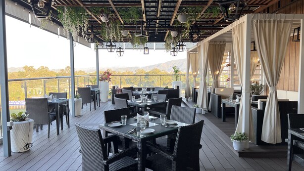 An outdoor restaurant with wicker furniture, hanging plants, and a view of the mountains. - Aurora Boutique Hotel (Imphal)
