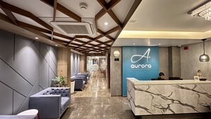 A modern hotel lobby with a marble reception desk, plush seating, and a blue wall with the hotel's logo. - Aurora Boutique Hotel (Imphal)