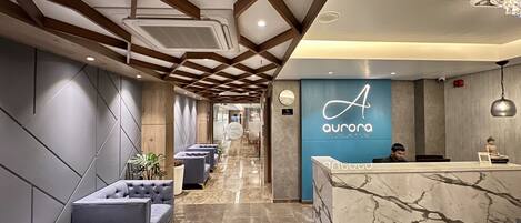 Un moderno vestíbulo de hotel con un mostrador de recepción de mármol, asientos lujosos y una pared azul con el logotipo del hotel.
