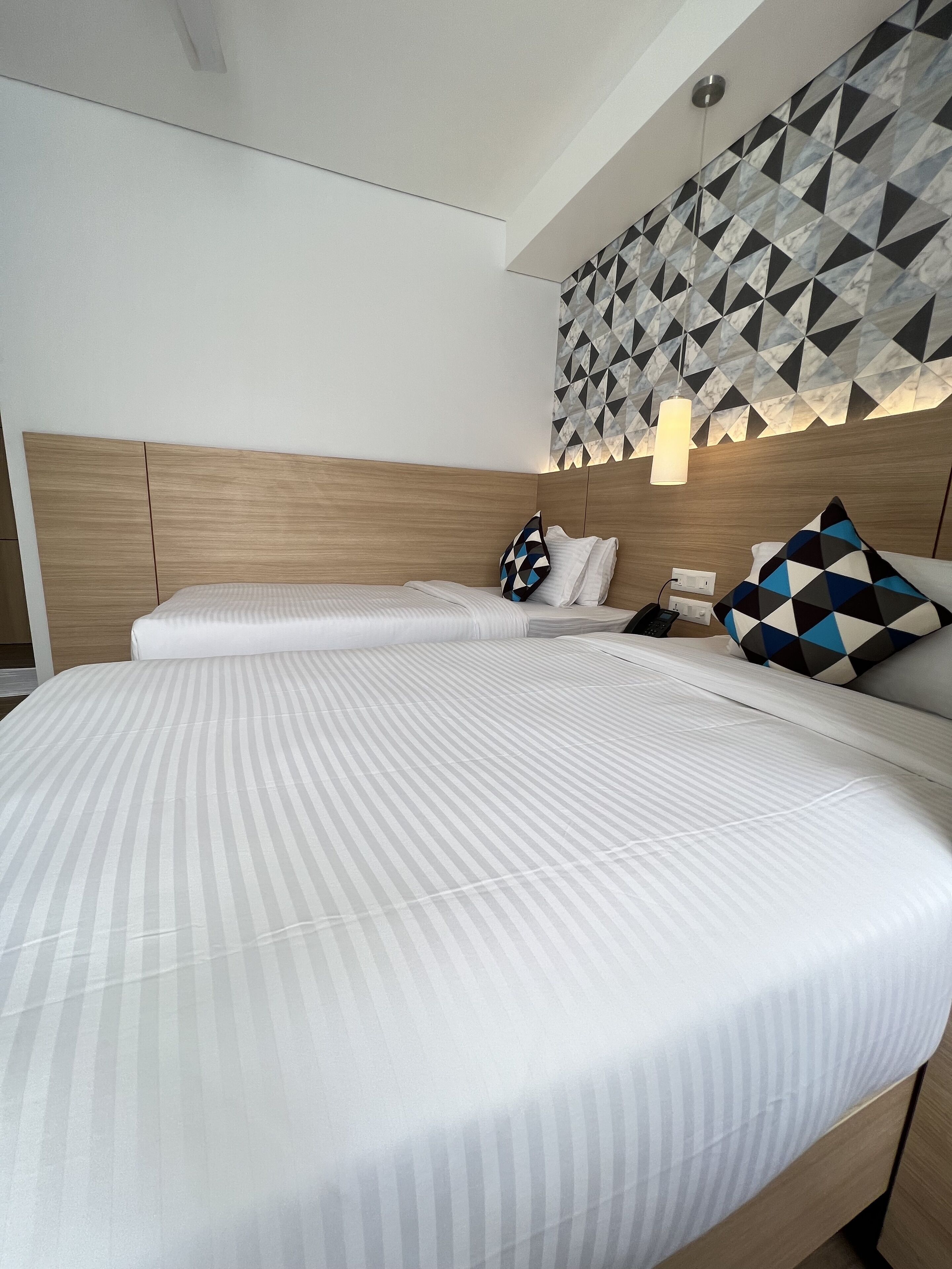 Een moderne hotelkamer met een groot bed, een houten hoofdbord en een wand met een geometrisch patroon boven het bed.