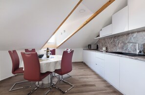 A modern kitchen with white cabinets, a marble backsplash, and a dining area with a round table and red chairs.