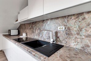 A modern kitchen with a black sink, white cabinets, and a marble backsplash.