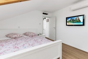 A bedroom with a bed, a nightstand, a TV on the wall, and a door leading to another room.