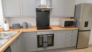 Una cocina moderna con armarios grises, un refrigerador de acero inoxidable, un microondas, un tostador y una tetera.