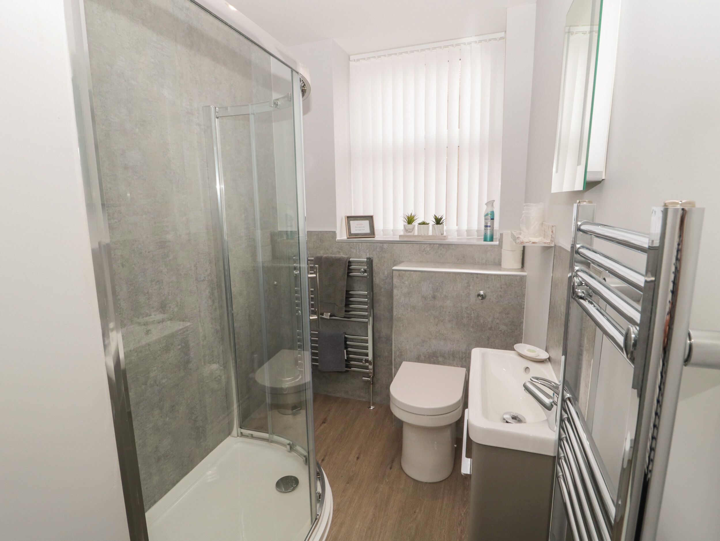 A modern bathroom with a glass-enclosed shower, a toilet, and a sink with a towel rack.