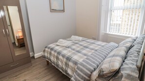 Un dormitorio con cama, armario, mesita de noche con lámpara y ventana con persianas.