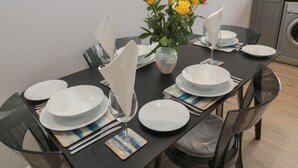 Una mesa de comedor con platos blancos, servilletas y cubiertos, y un florero con flores amarillas y rojas en el centro.