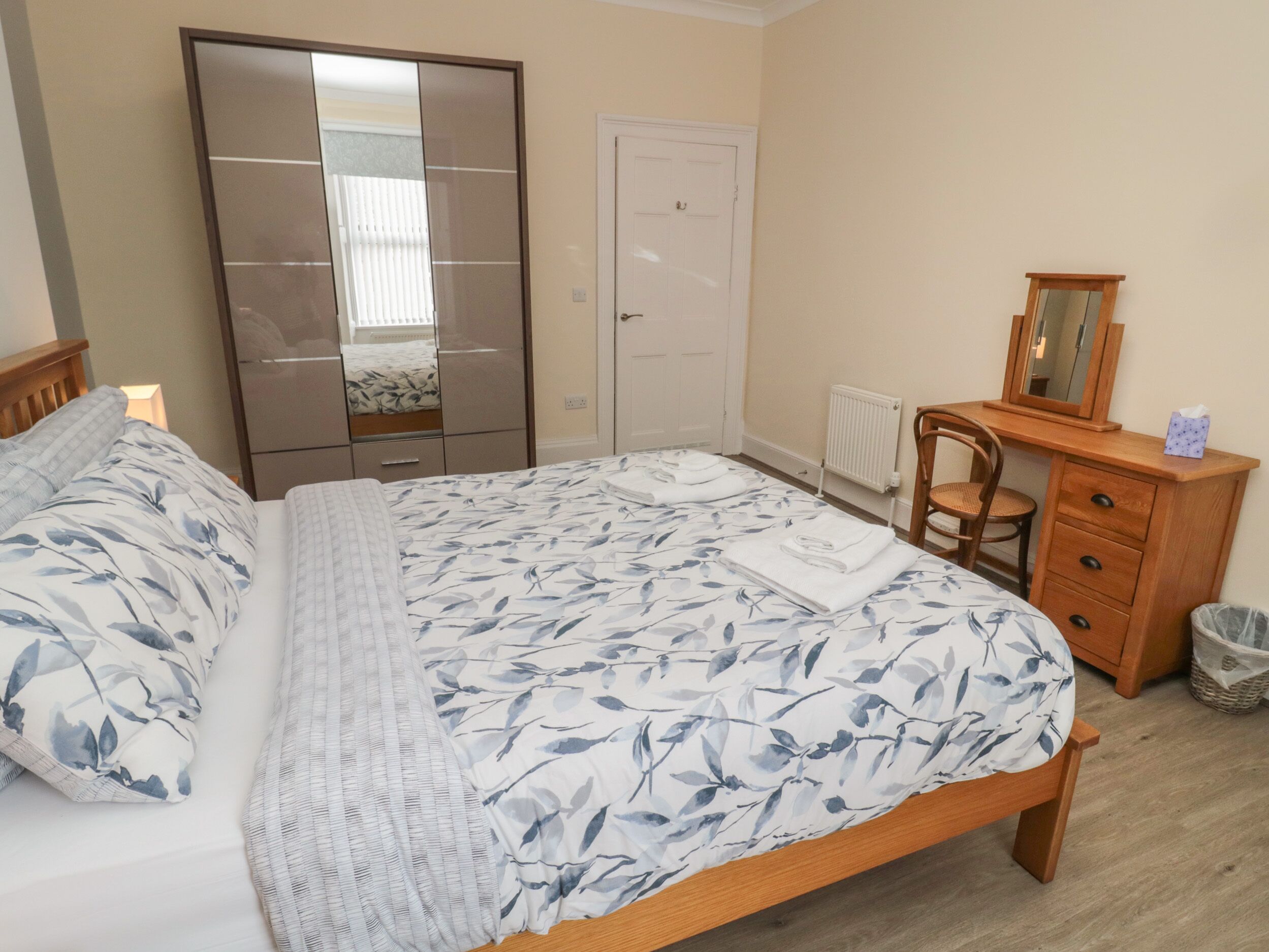 Un dormitorio con cama, armario, cómoda, silla y espejo.