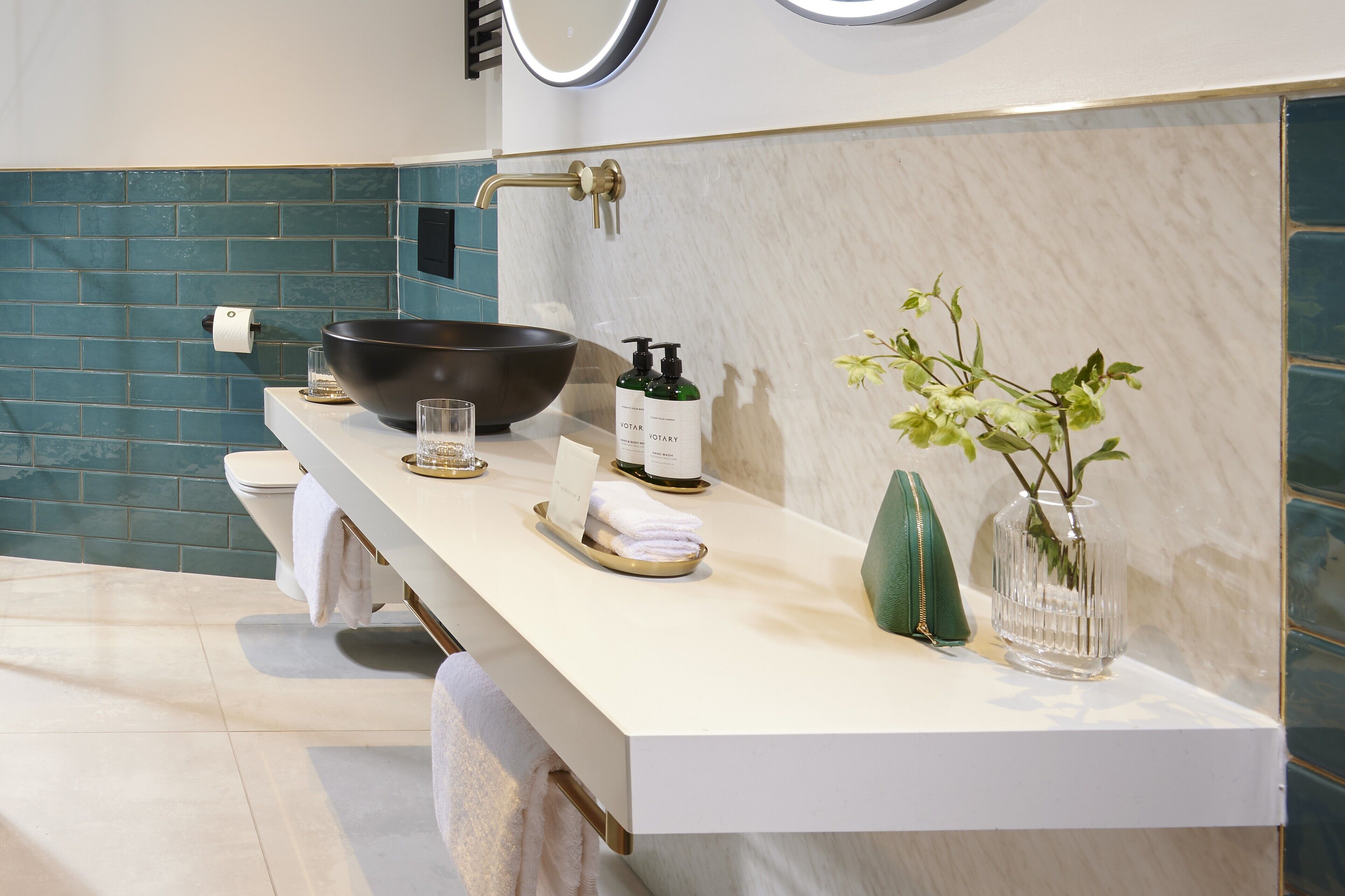 A modern bathroom with a white vanity, a black basin, a green plant, and a bottle of hand soap.