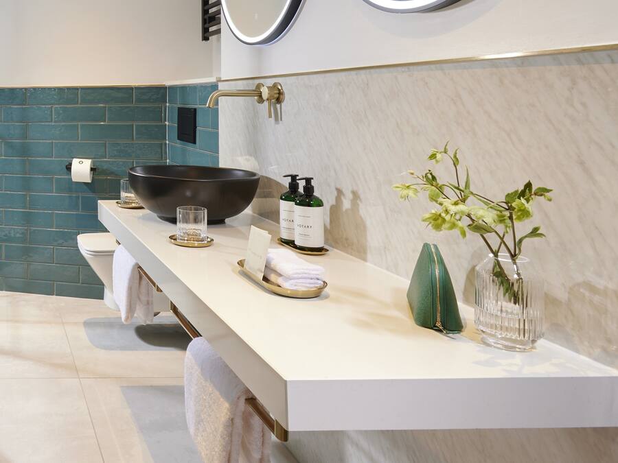 A modern bathroom with a white vanity, a black basin, a green plant, and a bottle of hand soap.