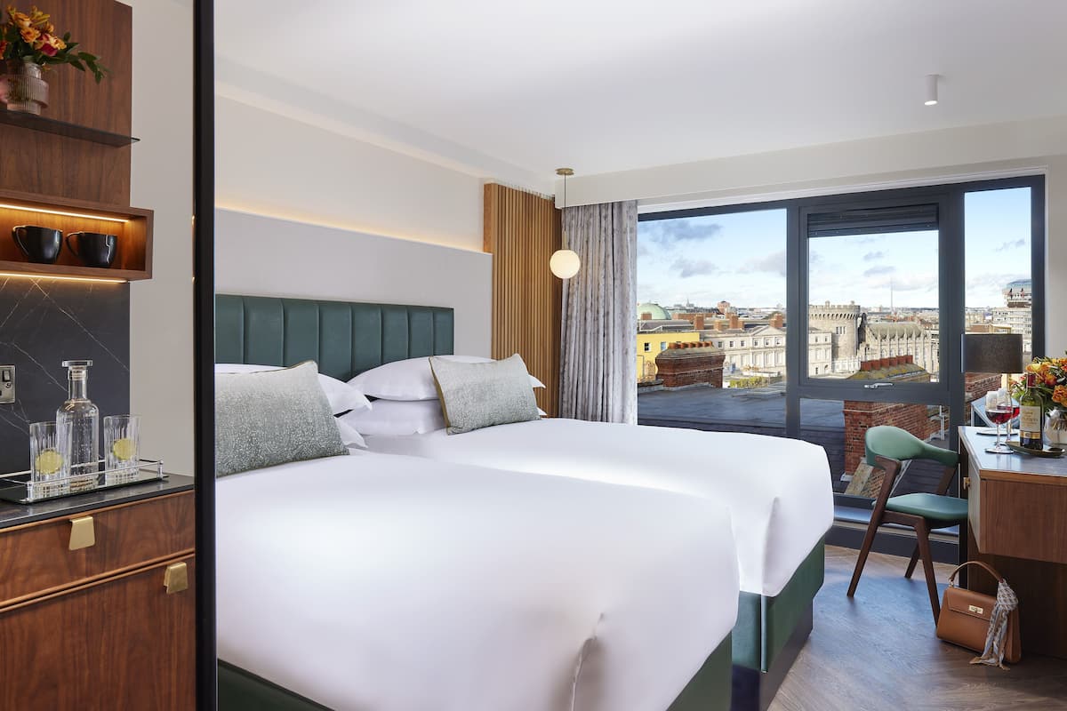 Ein Hotelzimmer mit einem großen Bett, einem Schreibtisch mit Stuhl, Blick auf die Stadt und einer Minibar.
