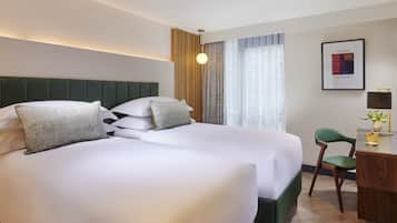 Une chambre d’hôtel avec deux lits, un bureau, une chaise, une lampe et un tableau encadré au mur.