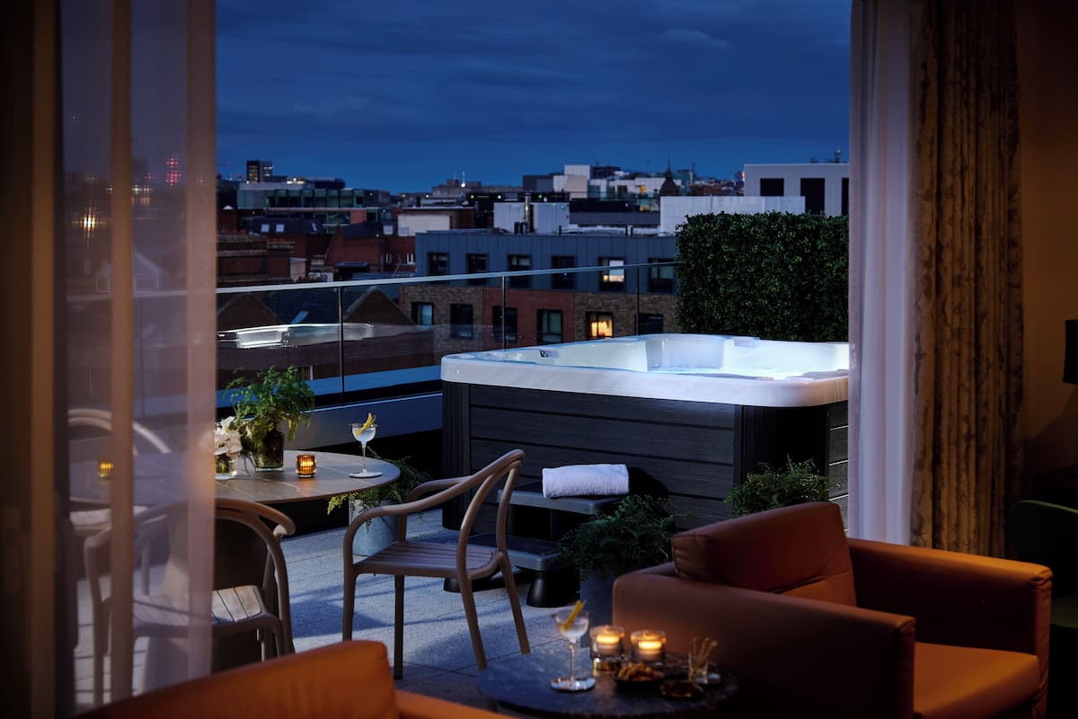 Eine Dachterrasse mit Whirlpool, Sitzgelegenheit und Blick auf die Stadt.