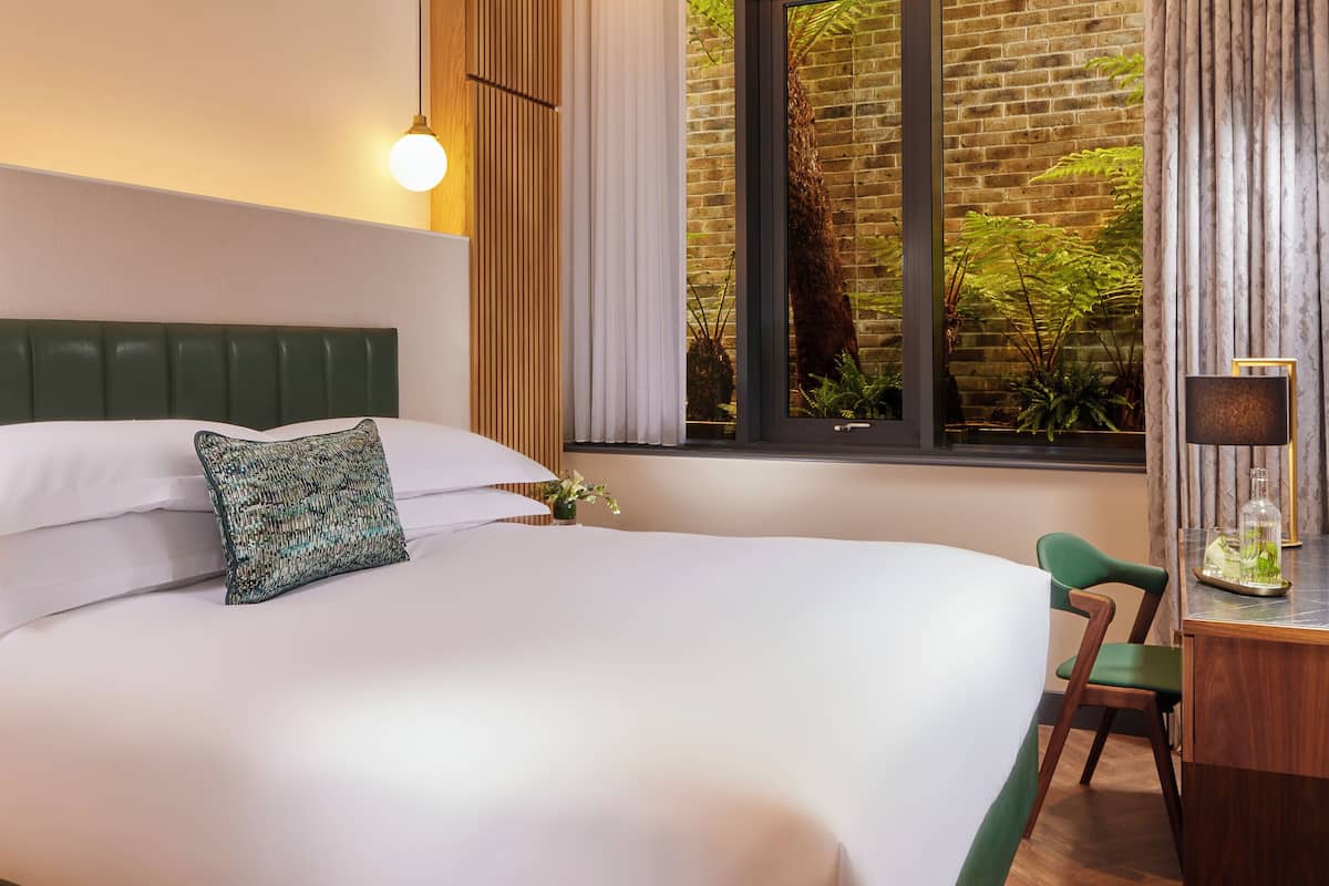 Ein modernes Hotelzimmer mit einem großen Bett, einem Schreibtisch und Blick auf Grün hinter dem Fenster.