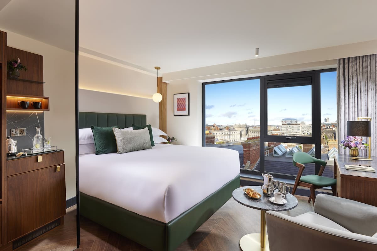 Ein modernes Hotelzimmer mit einem großen Bett, einem kleinen Tisch mit Frühstück, Blick auf die Stadt und einem Balkon.