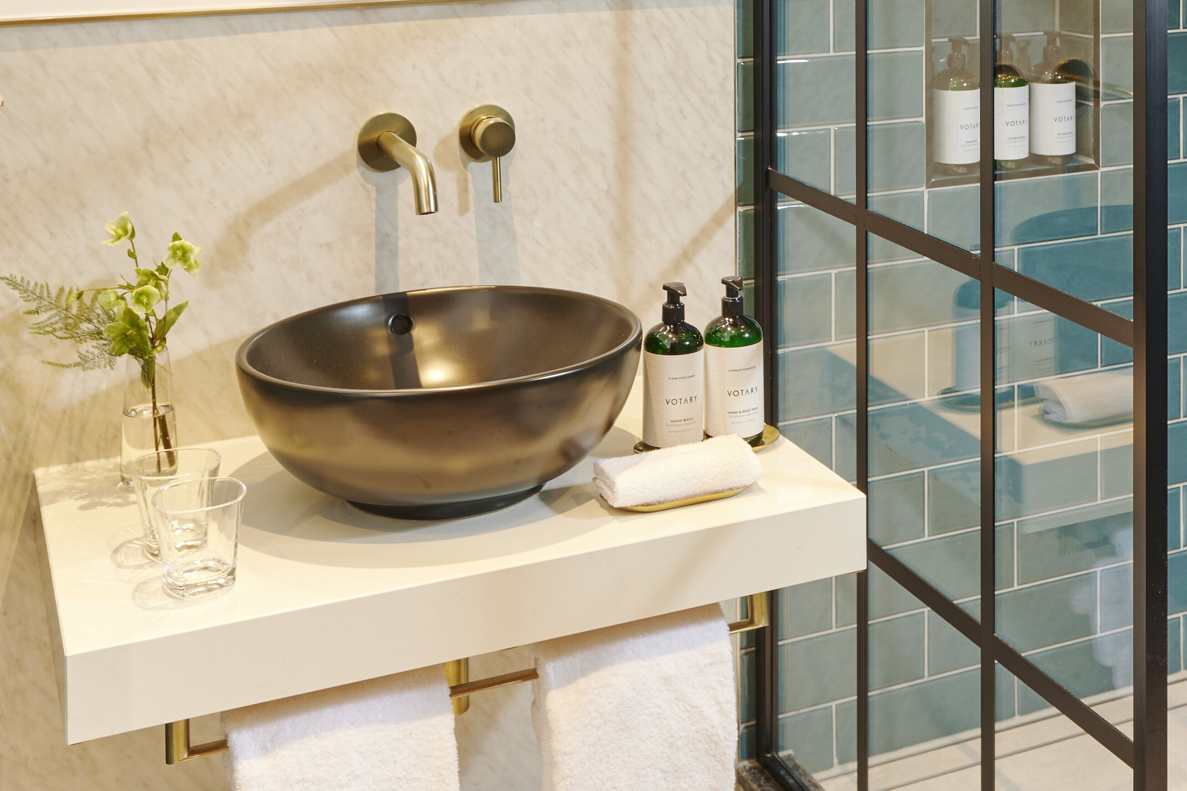 Une salle de bain moderne avec un grand lavabo sur pied, un vase en verre rempli de fleurs et des articles de toilette disposés sur le comptoir.