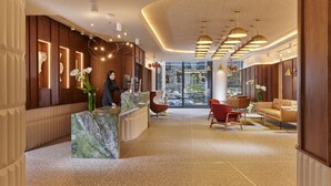 A modern reception area with a marble counter, wooden paneling, and a seating area with red chairs and a sofa. - The Chancery Hotel (Dublin)