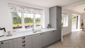 A modern kitchen with grey cabinets, a white countertop, and a large window overlooking a garden.