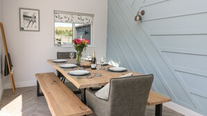 A dining area with a wooden table set for four, a vase with flowers, and a mirror above the table.