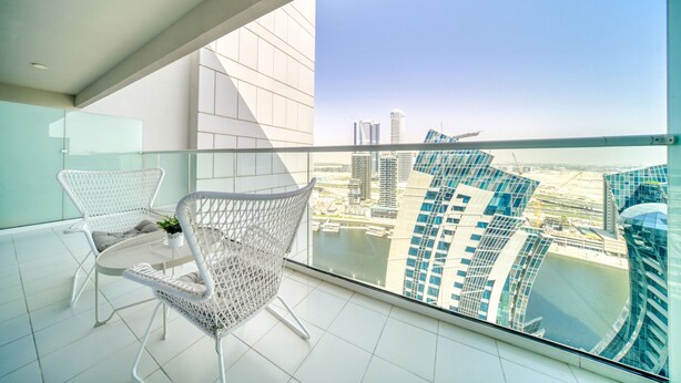 Un balcone con mobili in vimini bianco, vista su edifici moderni e cielo sereno.