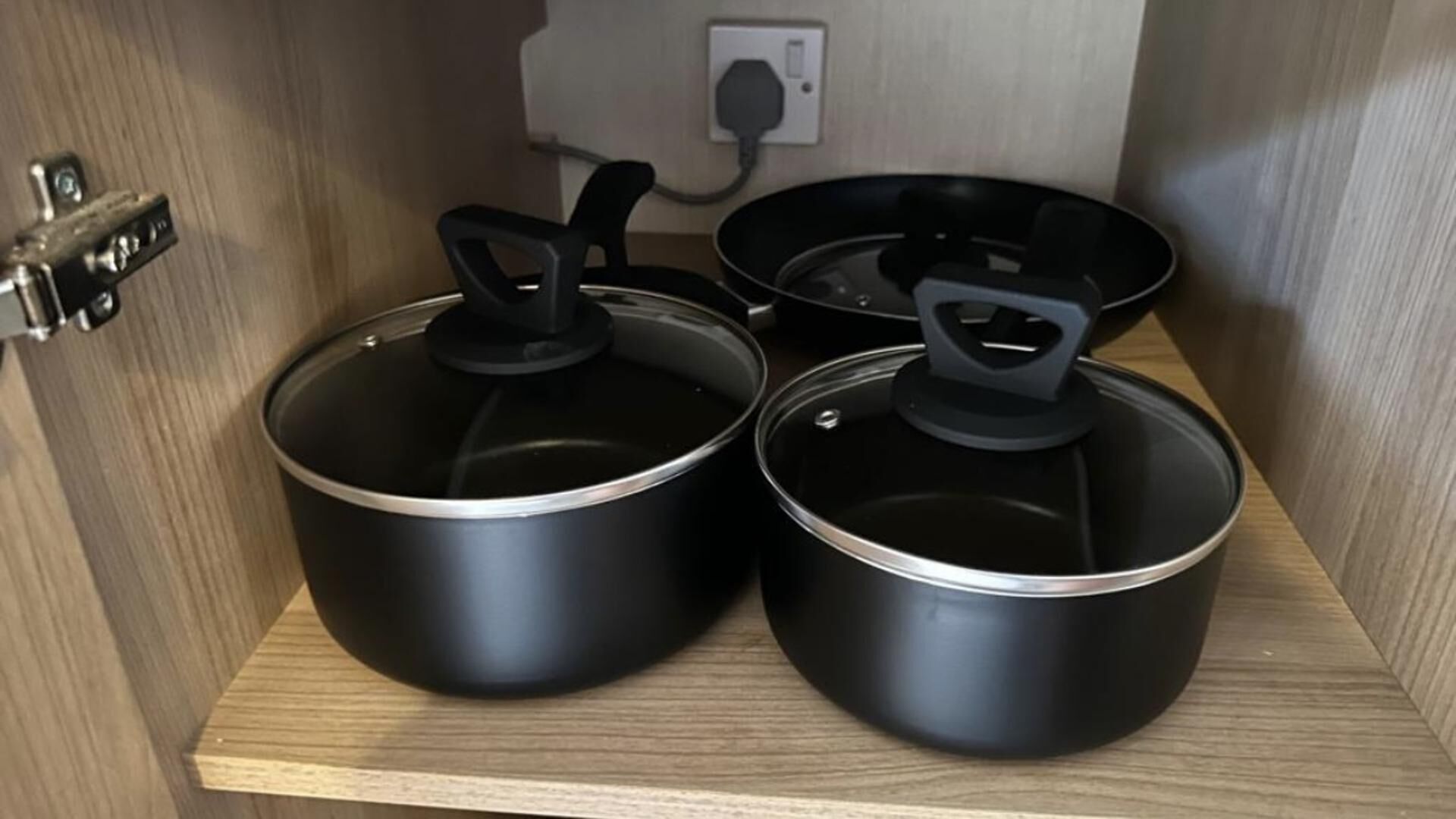 A kitchen with three black pots on a wooden shelf.