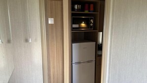 A compact kitchen with a refrigerator, microwave, and a shelf with various items. - 3-bed Caravan Near Mablethorpe (Louth)