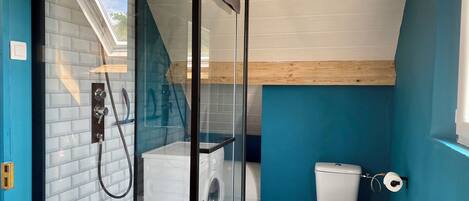 A modern bathroom with a glass-enclosed shower, a white toilet, and a washing machine.