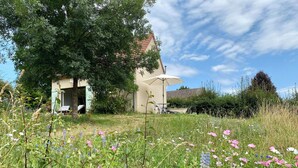 Een huis met een tuin ervoor, een terras met tuinmeubilair en een heldere lucht.