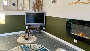 Een woonkamer met een flatscreen televisie, een open haard en een eethoek met een tafel gedekt voor twee personen.