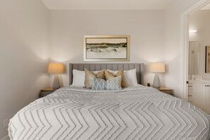 A neatly made bed with a patterned bedspread, two bedside lamps, and a framed artwork above the bed.