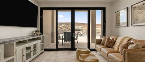 Uma sala de estar com sofá, mesa de centro, televisão e porta de vidro deslizante que dá para um pátio externo.