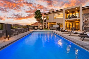 A swimming pool with lounge chairs and a modern house with a balcony.