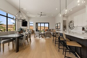 A spacious living area with a large window, a dining area with a kitchen counter, and a ceiling fan.