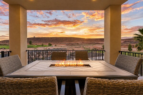 An outdoor patio with a fire feature, wicker furniture, and a view of a desert landscape.