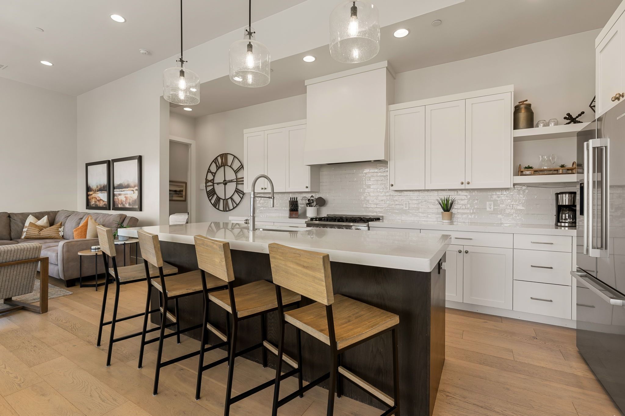A modern kitchen with white cabinetry, a large island with bar stools, and pendant lighting.
