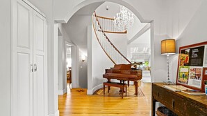 Un piano de cola en una habitación amplia con suelo de madera, una araña de cristal y un cuadro en un mueble de madera.